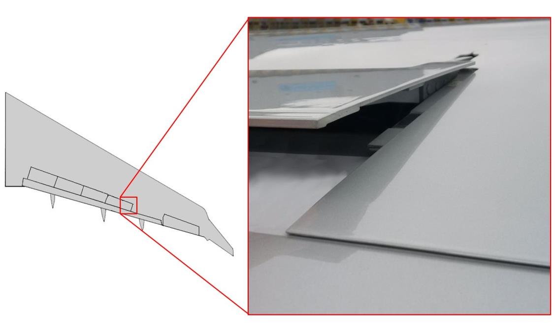 Photograph of the right outboard spoiler panel standing slightly raised above the wing surface, with an inset outline of the wing marking where the panel sits.