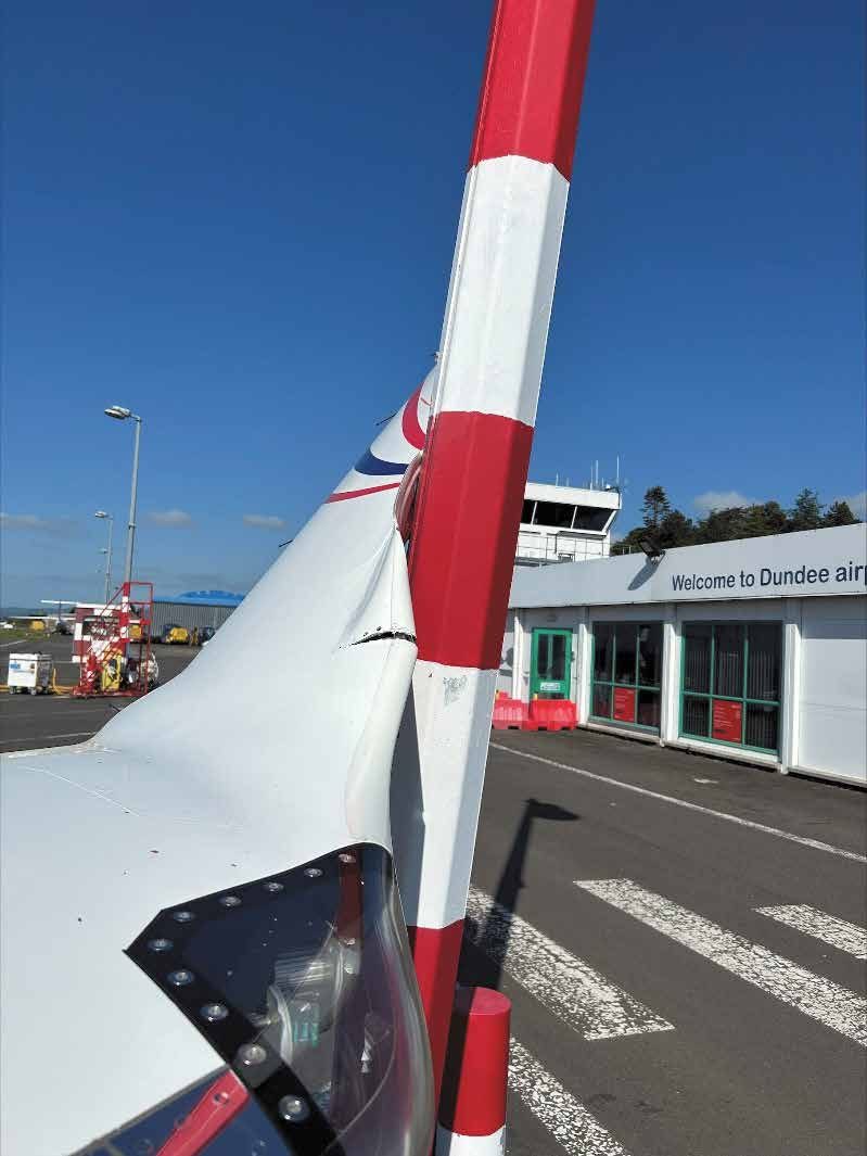 Close view of the left winglet touching a red and white striped lamppost, with the skin of the winglet creased where it meets the post.